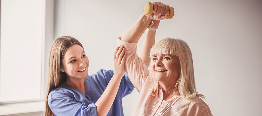 therapist helping elderly woman do arm exercises